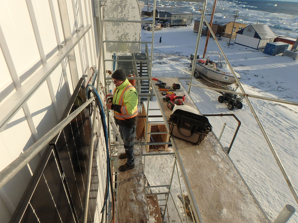 Michael Schneider working on installing solar panel on side of a buidling.