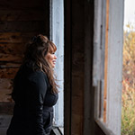 Marilyn standing in front of the window of her grandparent’s cabin, looking outside.