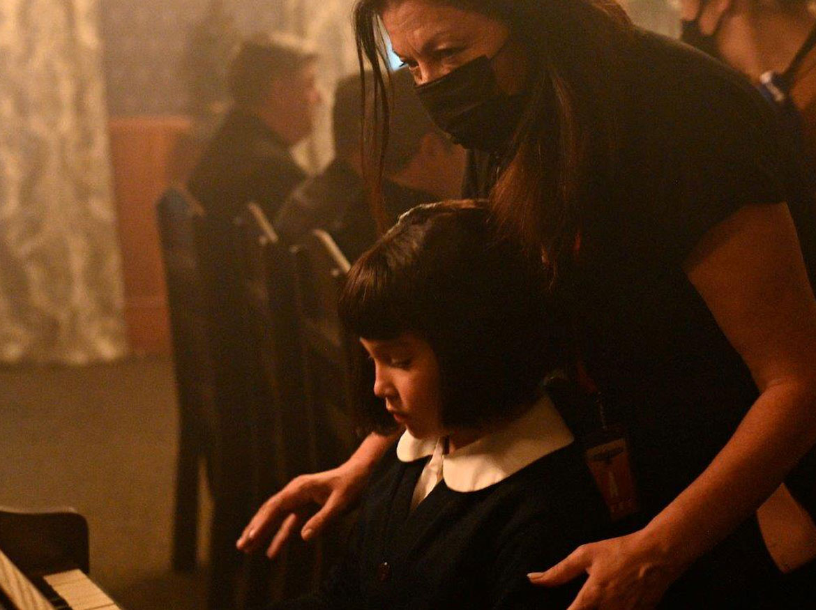 Director Marie Clements standing behind child actor playing piano.