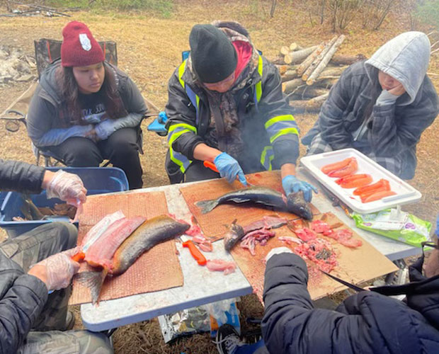 Groupe de jeunes assis autour d'une table observant un homme qui nettoie et prépare un poisson