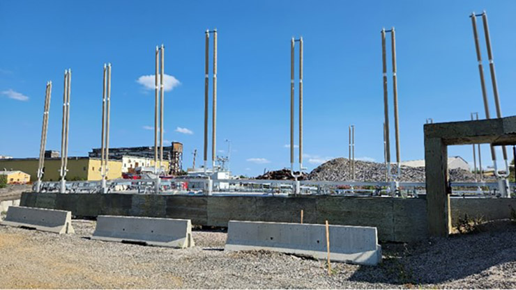 Une série de grands poteaux métalliques dépassent d'un bloc de béton sur un site industriel.