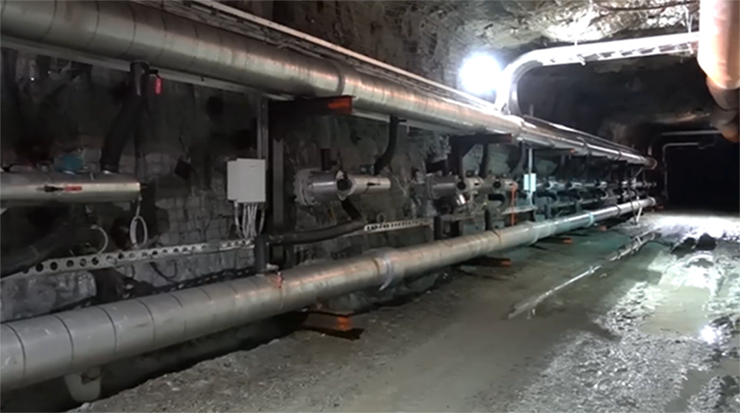 A view of an underground mine chamber showing a damp ground and pipes running along the left side.