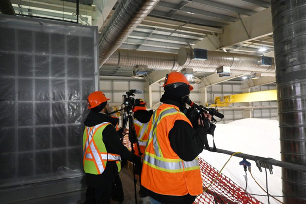 Trois personnes portant des casques et des gilets de sécurité prennent des photos et des vidéos à l'intérieur d'un bâtiment encore en construction.