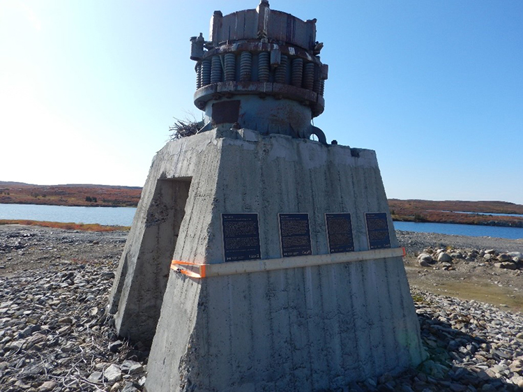 4 commemorative plaques in Tłı̨chǫ (Dogrib), Wıı̀lıı̀deh Yatı, English, and French languages installed on an old pyramid-shaped rock crusher