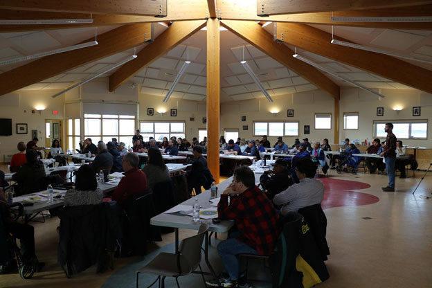 Cette photo montre une salle pleine de gens assis à des tables lors d'une réunion.